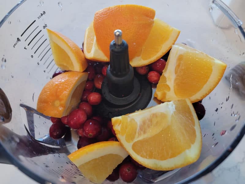 orange chunks, cranberries in the bowl of a food processor for cranberry relish
