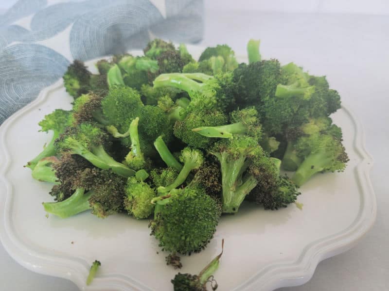 Air fried broccoli on a white plate next to a cloth napkin