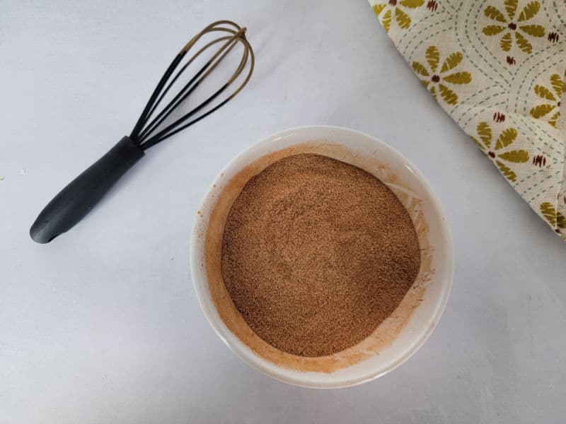 Cinnamon Sugar in a white bowl next to a whisk and cloth napkin