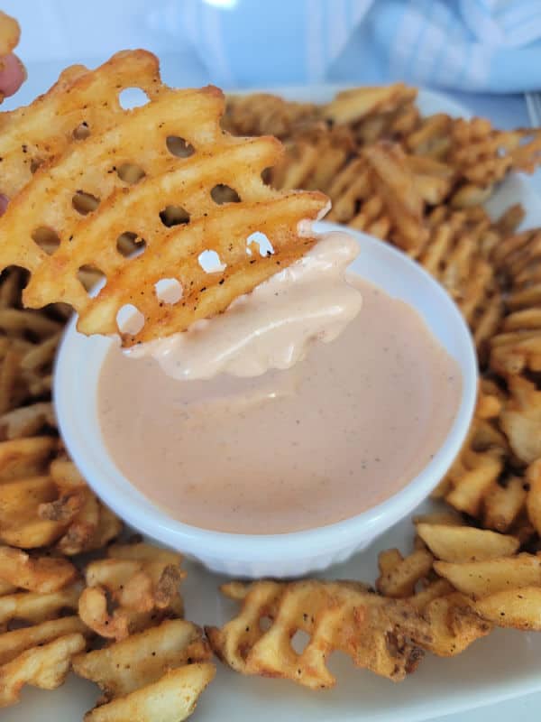 Waffle fry dipping into Comeback sauce in a white bowl surrounded by fries