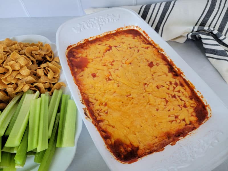 Franks Buffalo Chicken Dip in a white casserole dish next to celery and Frito Chips