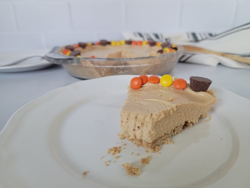 Slice of peanut butter pie on a white plate with the baking dish behind it