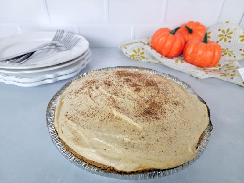 No bake pumpkin pie in a pie dish next to mini pumpkins and a stack of plates and forks. 