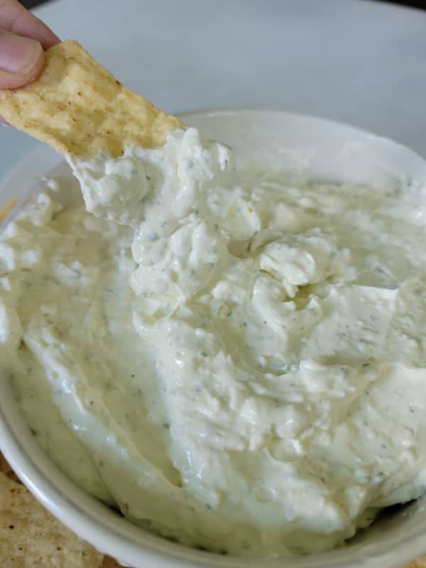 Tortilla chip dipping into ranch dip in a white bowl