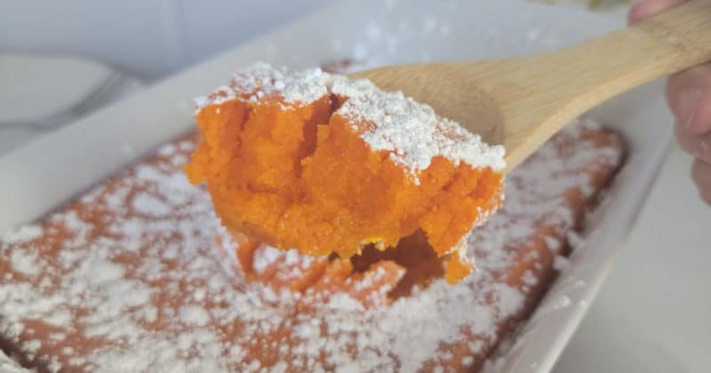 carrot souffle on a wooden spoon above a casserole dish