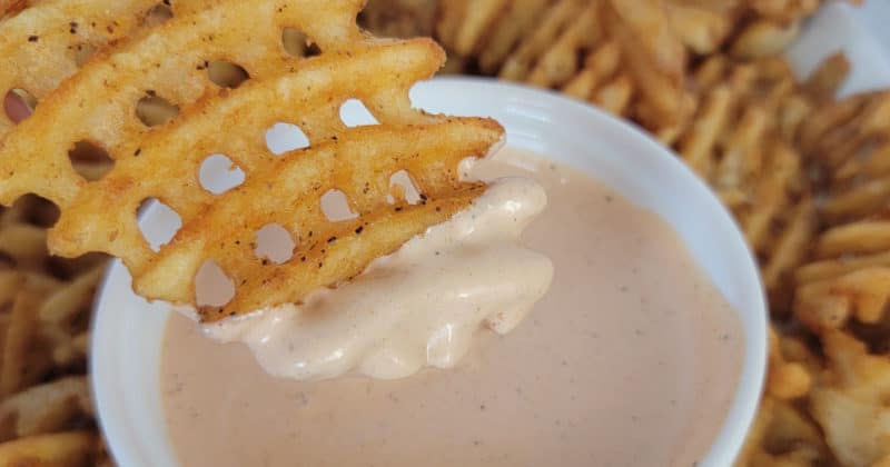 Waffle french fry dipping into comeback sauce in a white bowl