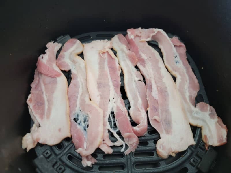 uncooked bacon spread on an air fryer basket