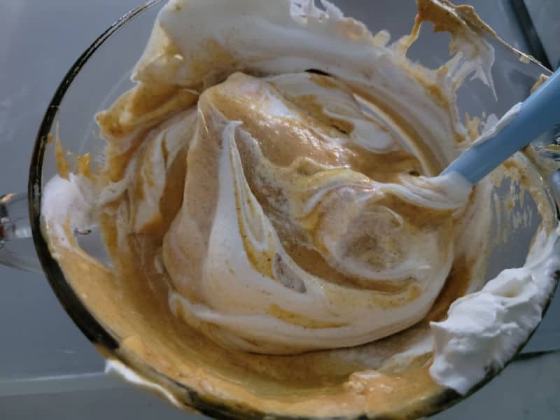 Cool whip mixing into no bake pumpkin pie filling in a glass bowl with a spatula