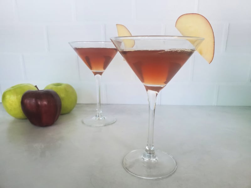 Two Washington Apple Cocktails in martini glasses with apple slice garnish next to red and green apples. 