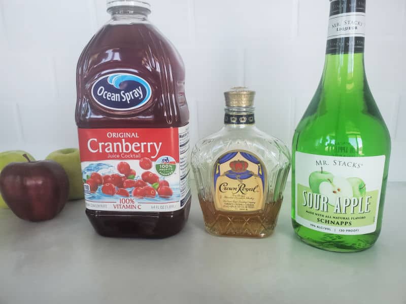 red and green apples next to a bottle of cranberry juice, crown royal, and sour apple schnapps