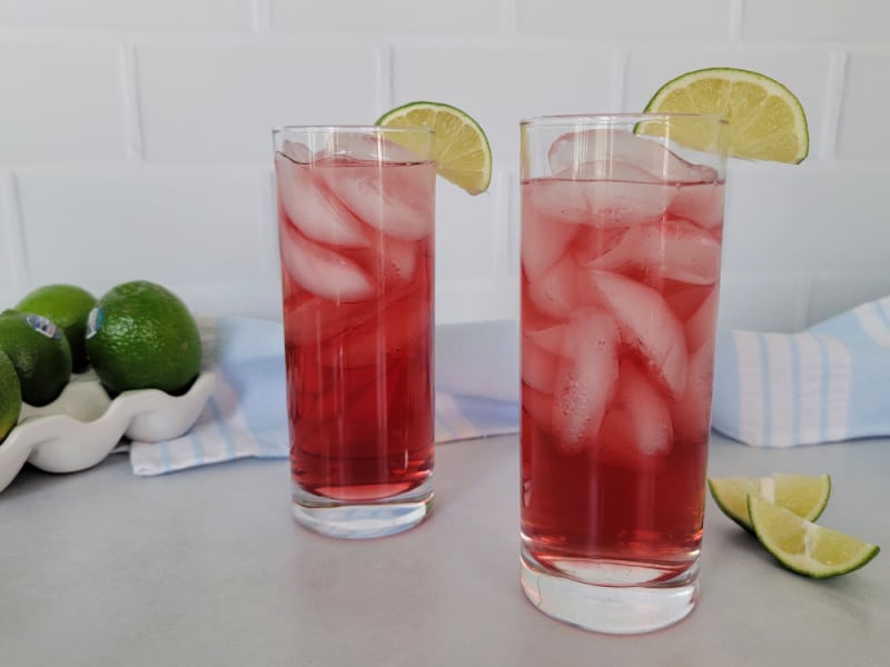 2 Woo Woo cocktails in tall glasses with lime wedge garnish next to a pile of limes