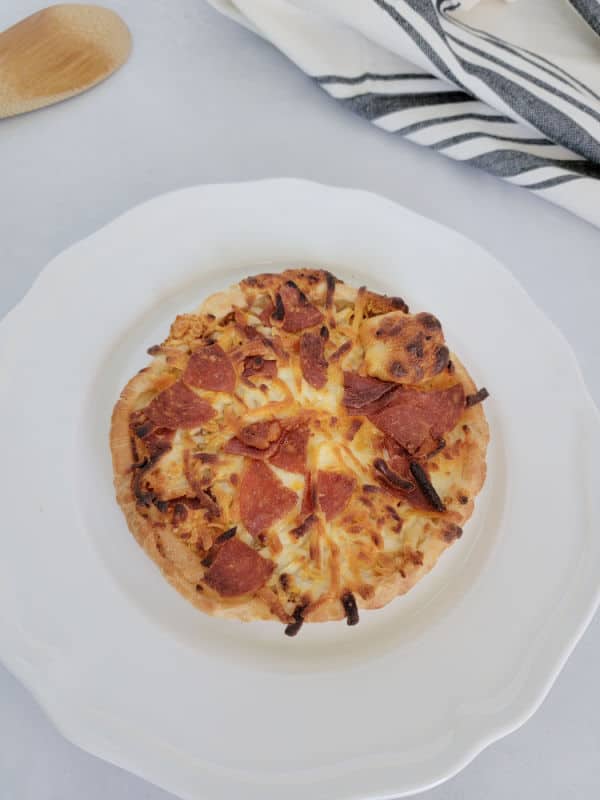 Air fried pepperoni pizza on a white plate near a cloth napkin