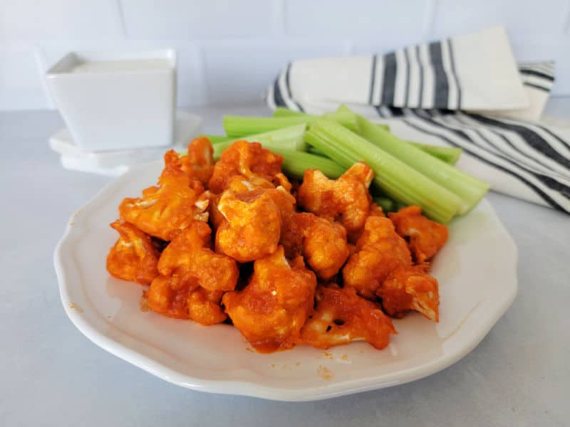 Air fried buffalo cauliflower on a white plate with celery sticks next to a napkin