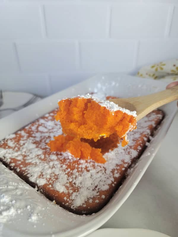 Carrot Souffle on a wooden spoon being served from a casserole dish