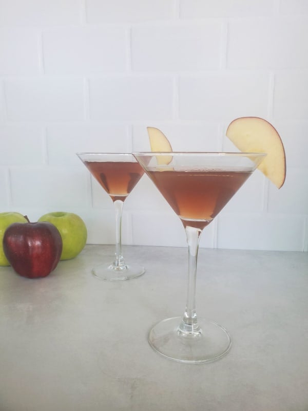 Two Washington apple drinks in martini glasses with apple slice garnishes next to red and green apples