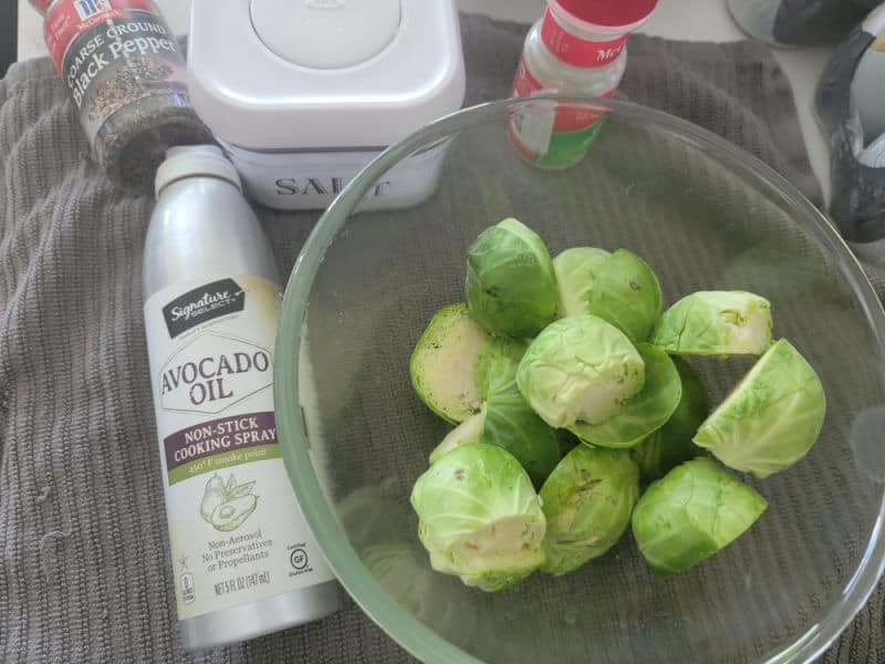 bowl of Brussel sprouts next to avocado oil, salt, pepper, and garlic powder