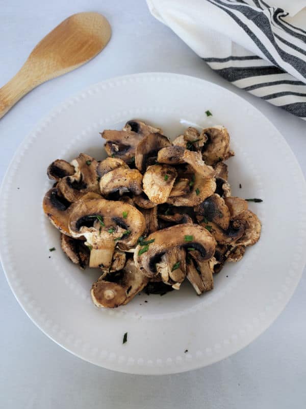 air fried mushrooms on a white plate next to a wooden spoon and cloth napkin