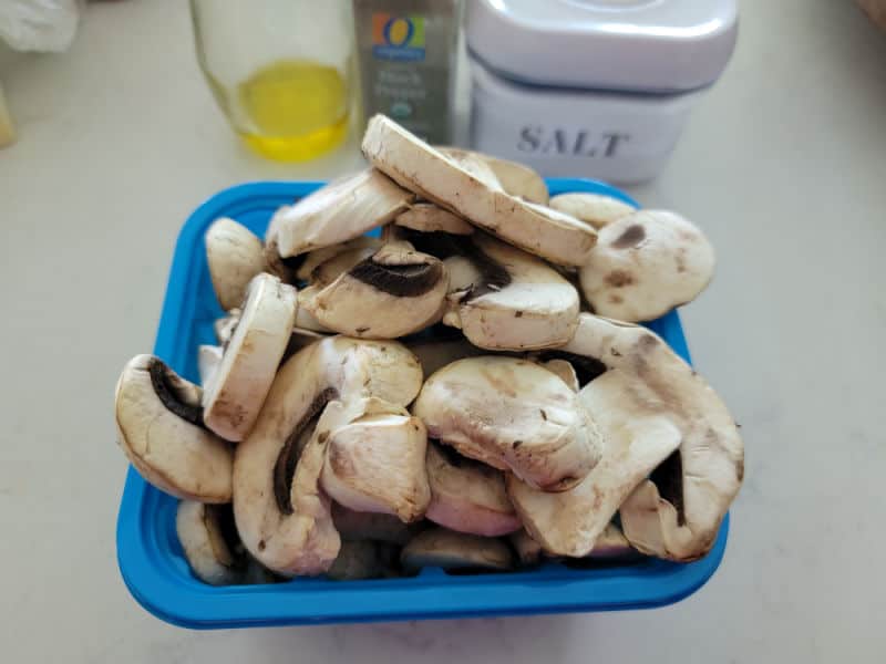 fresh mushrooms in a blue container next to olive oil, pepper, and salt