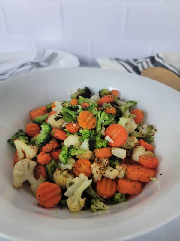 air fried broccoli and carrots with cauliflower on a white plate next to a wooden spoon and cloth napkin