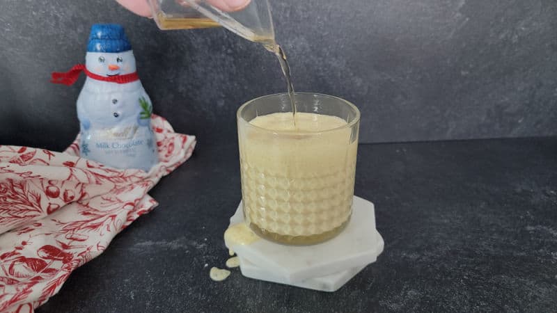 Bourbon pouring into a glass filled with eggnog for a bourbon eggnog cocktail