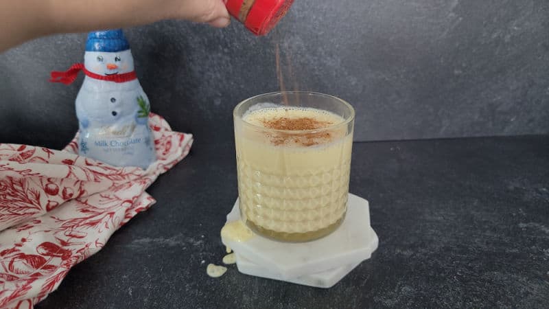 Nutmeg sprinkled over a bourbon eggnog cocktail in a crystal glass