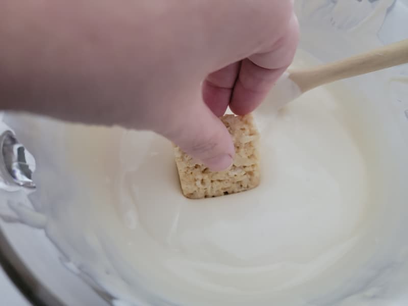 Rice Krispie treat dipping into a bowl of almond bark for Chocolate covered rice krispie treats