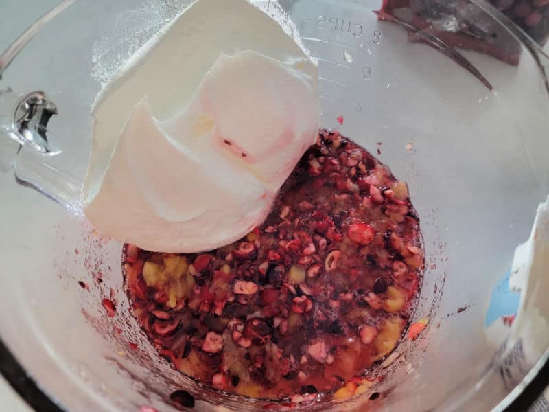 Cool whip in a glass bowl on pineapple pieces and shredded cranberries for cranberry salad