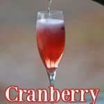 Cranberry Mimosa in a champagne glass with champagne pouring into the glass