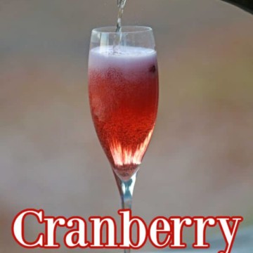 Cranberry Mimosa in a champagne glass with champagne pouring into the glass