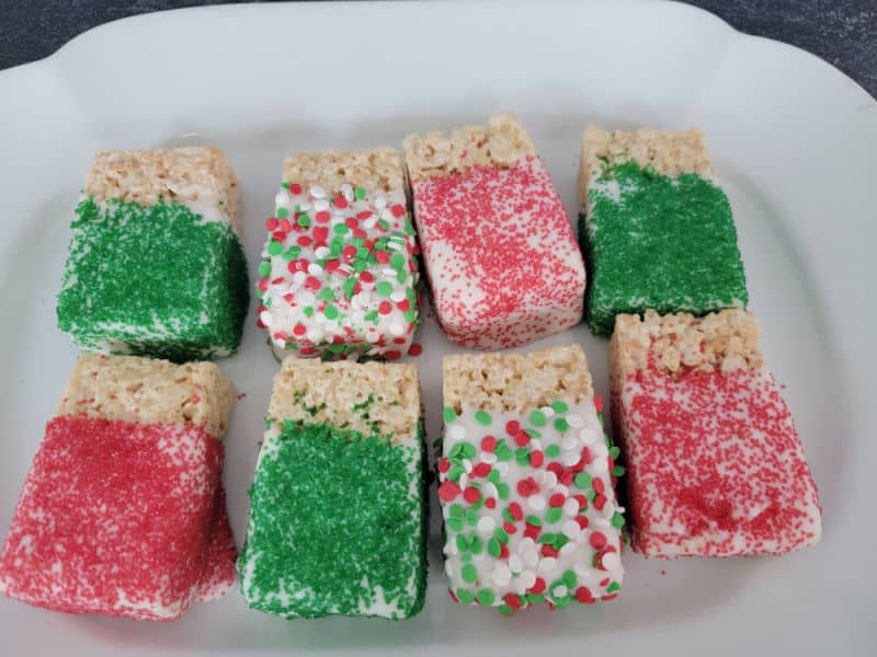 Chocolate covered rice krispie treats covered in holiday sprinkles on a white platter