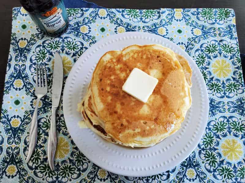 cracker barrel pancakes on a white plate with a square of butter, next to a fork, knife, and bottle of syrup