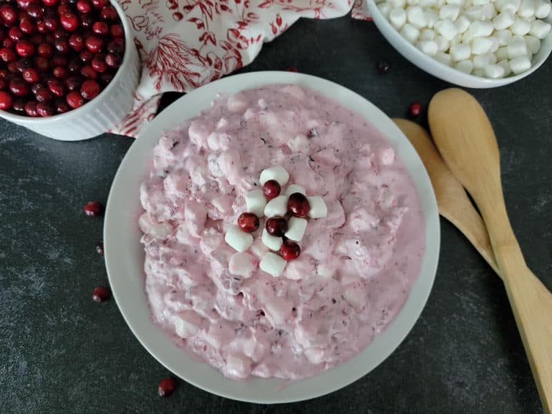 cranberry fluff salad in a white bowl next to a bowl of cranberries and mini marshmallows