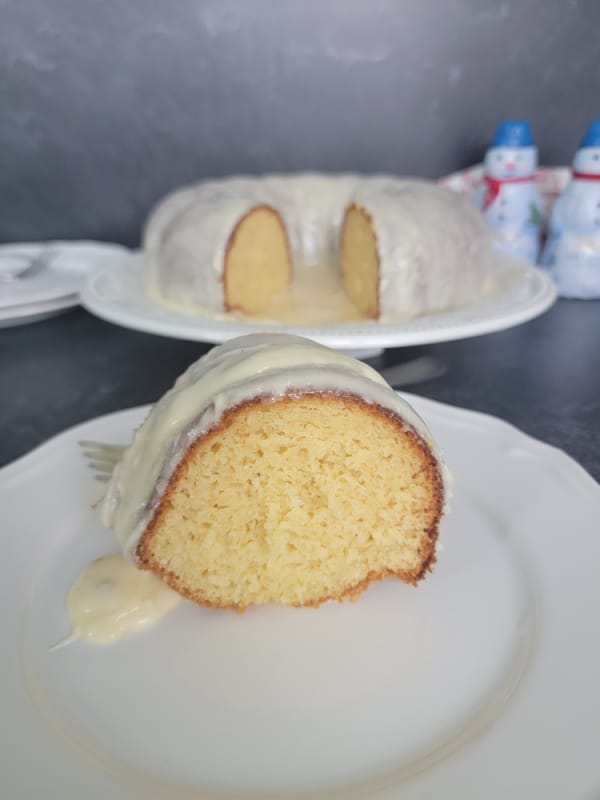 Slice of Eggnog cake covered in eggnog glaze on a white plate