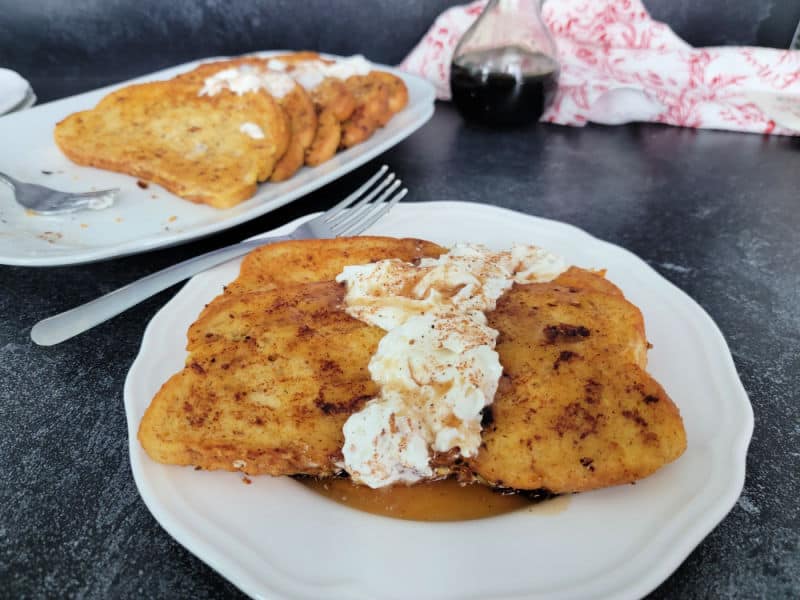 Eggnog French Toast slices on a white plate garnished with eggnog whipped cream and cinnamon/nutmeg