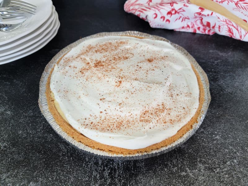 Eggnog pie garnished with cool whip and ground nutmeg on a dark counter with plates and forks