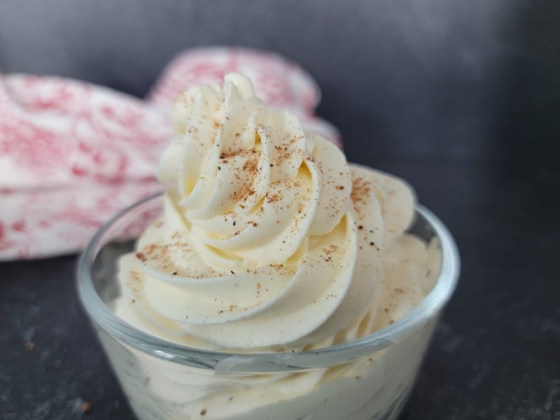 Eggnog Whipped Cream piped into a clear glass bowl garnished with ground nutmeg