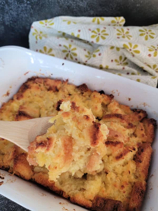 Wooden spoon serving pineapple stuffing from a white baking dish