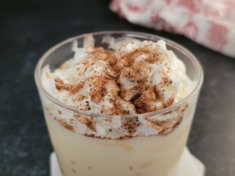 ground nutmeg on whipped cream at the top of an eggnog drink with a cloth napkin in the background. 
