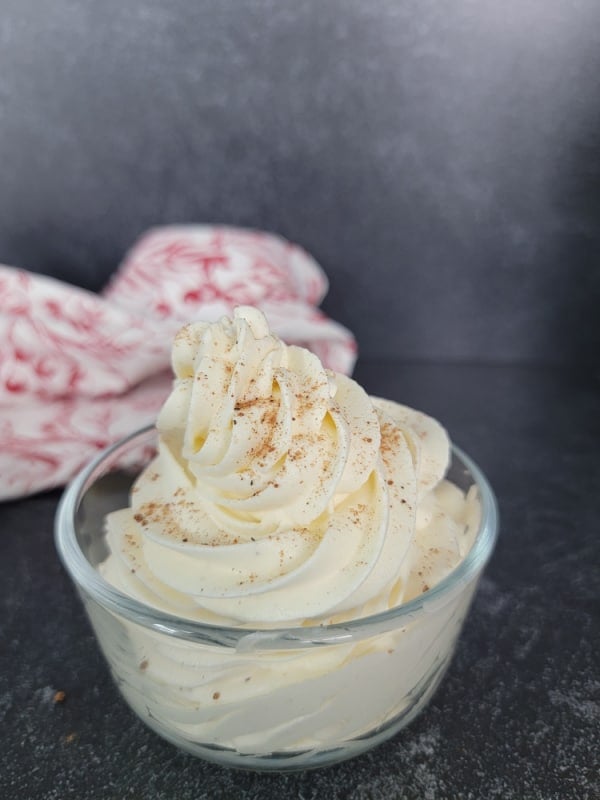 Eggnog Whipped Cream dusted with ground nutmeg in a clear glass bowl