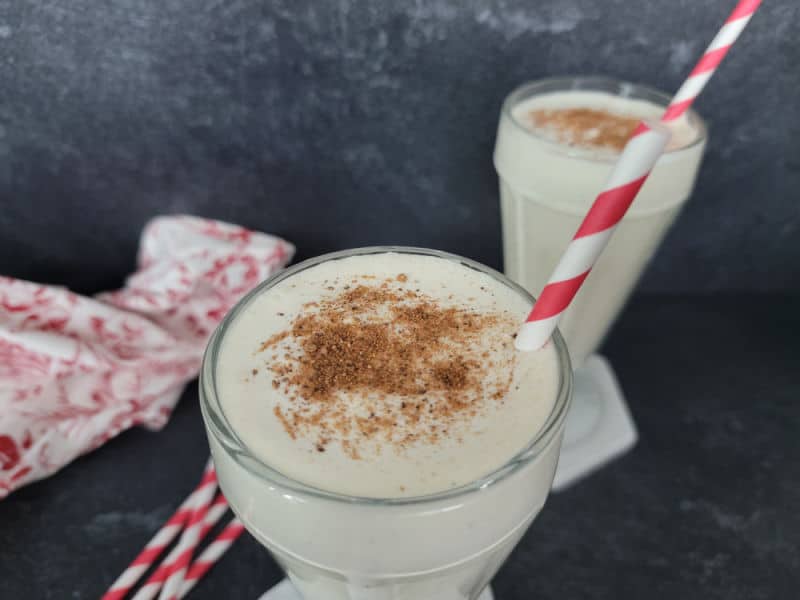 eggnog shake in a milkshake glass with ground nutmeg sprinkled on top with a red striped straw