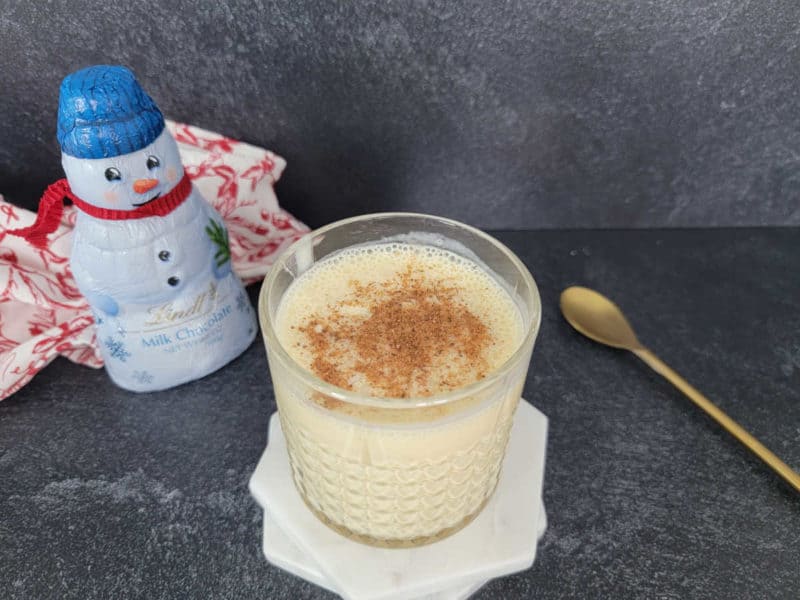 Bourbon Eggnog cocktail in a glass next to a snowman chocolate and gold spoon