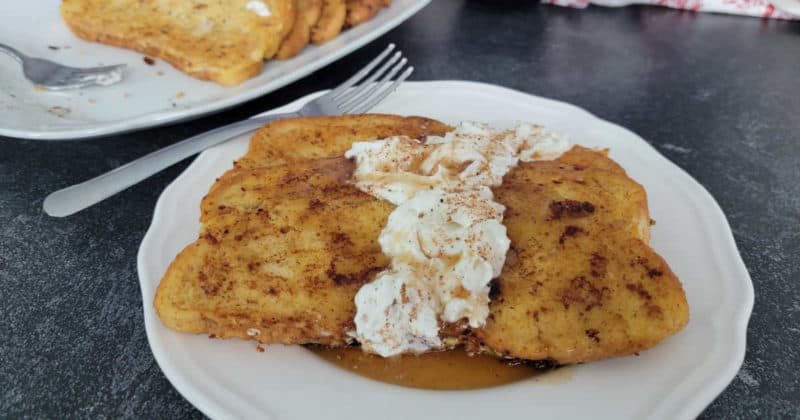 Eggnog French Toast with Eggnog Whipped Cream on a white plate with a silver fork