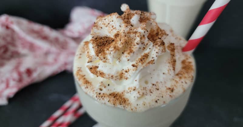 Creamy eggnog shake in a tall glass garnished with whipped cream and nutmeg