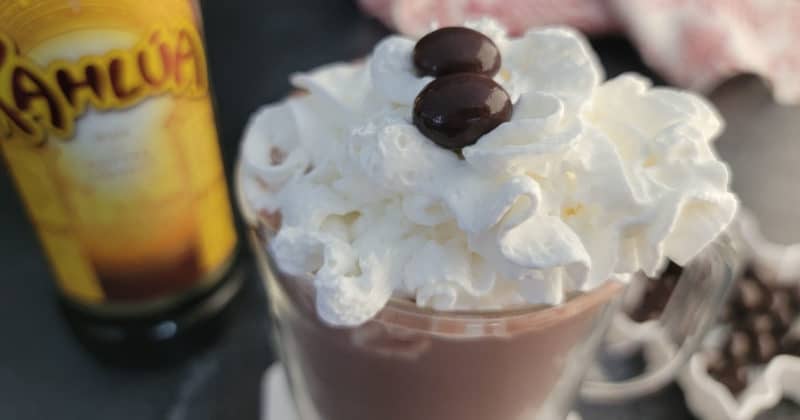 Kahlua Hot Chocolate with whipped cream in a glass mug next to a bottle of Kahlua