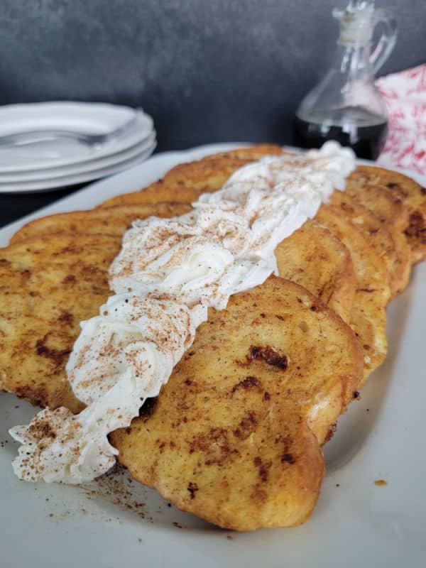 Eggnog French Toast slices on a white plate garnished with eggnog whipped cream and cinnamon/nutmeg