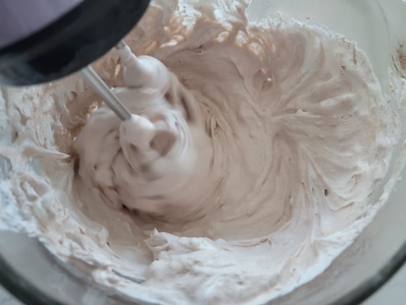 Hand mixer mixing hot cocoa mix ingredients in a glass bowl