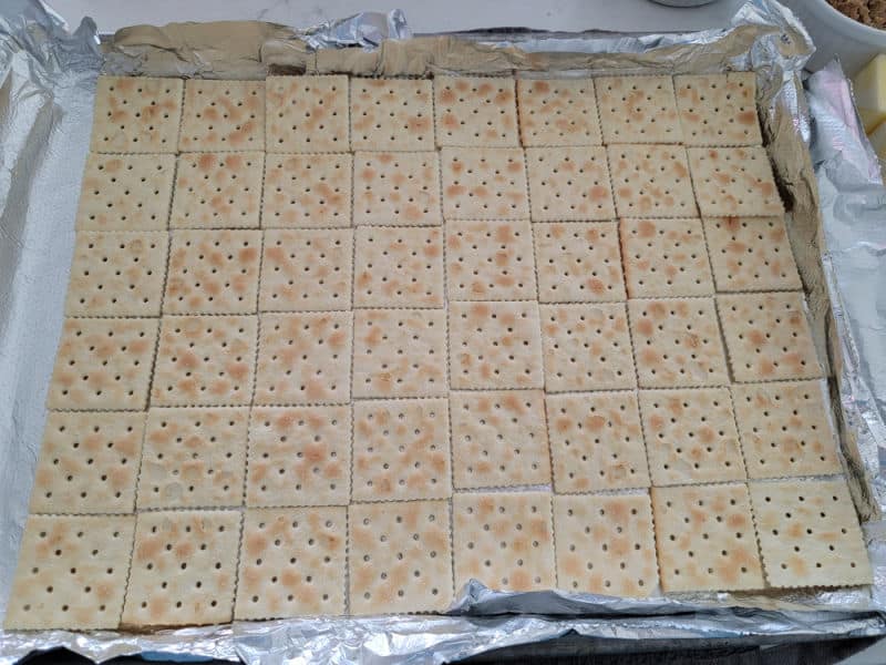 Saltine crackers spread on an aluminum foil lined baking dish for Christmas Crack Saltine Toffee