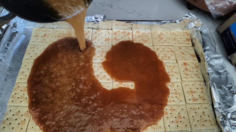 Toffee mixture pouring over saltine crackers for Christmas Crack