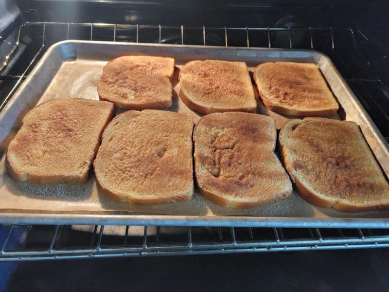 Cinnamon sugar covered toast on parchment paper lined baking sheet in the oven. 