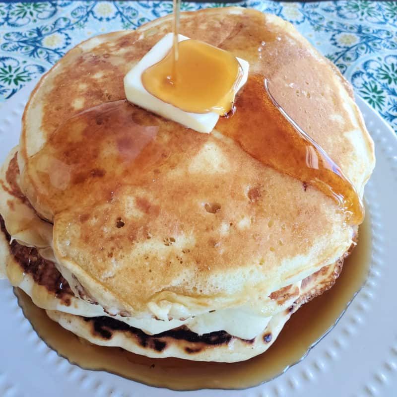 stack of cracker barrel pancakes on a white plate with syrup dripping over the pancakes